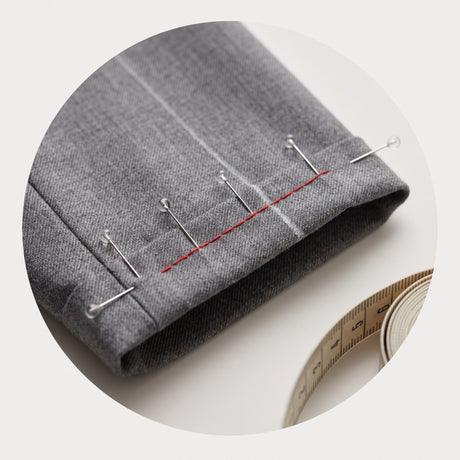 Pinned trouser hem with red basting stitch and a tape measure